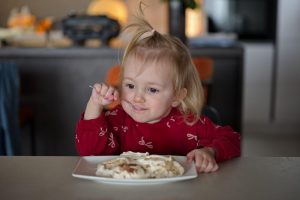 majhna deklica sedi za mizo in je torto