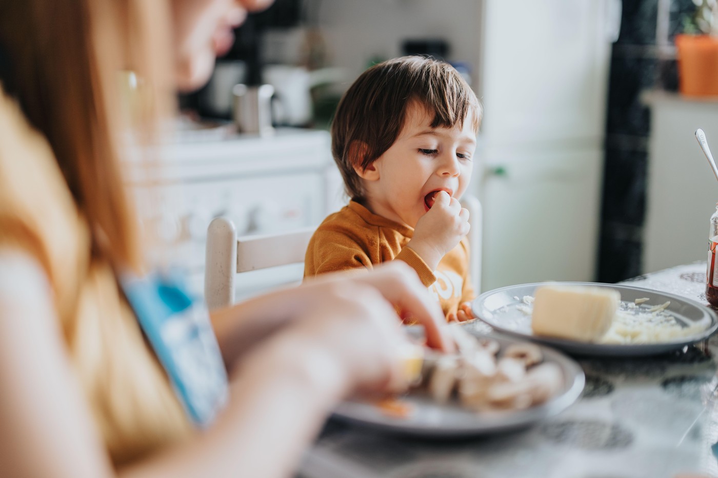 otrok sedi za mizo, s prsti nosi hrano v usta