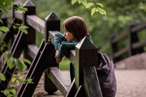 deček z nahrbtnikom sredi parka naslonjen na ograjo strmi v naravo