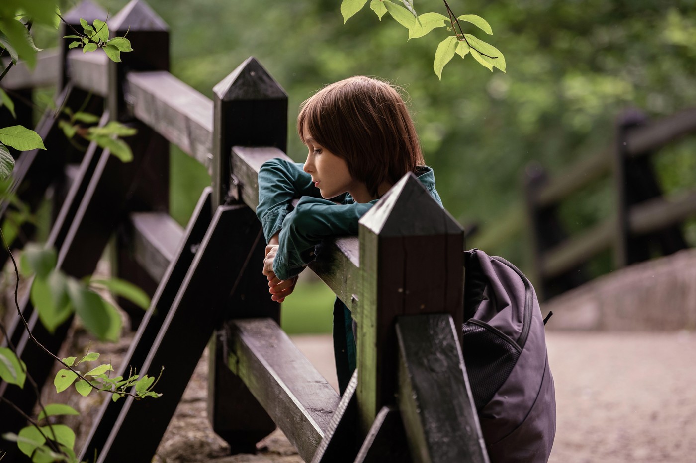 deček z nahrbtnikom sredi parka naslonjen na ograjo strmi v naravo