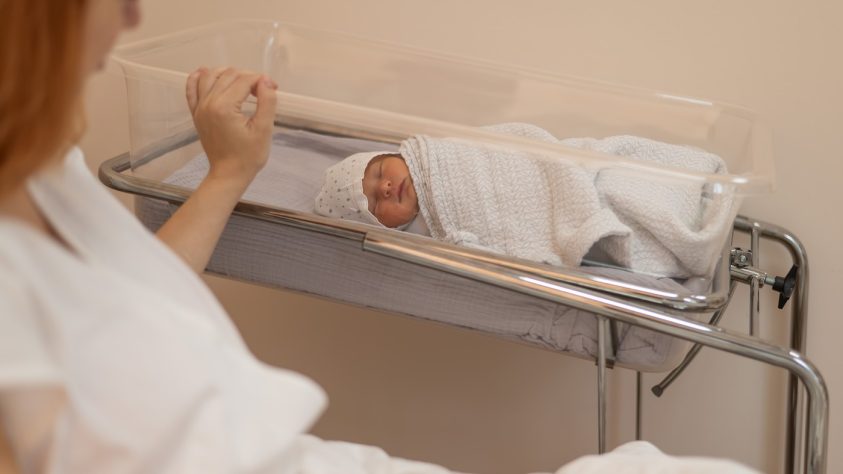 mama po porodu v porodnišnici gleda otroka, ki leži v posteljici