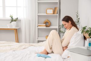 mlada ženska sedi v bolečinah na postelji