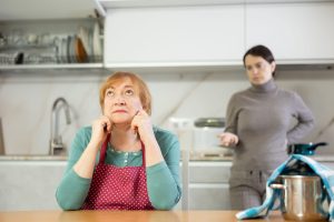 starejša ženska sedi za mizo, mlajša ženska je v ozadju