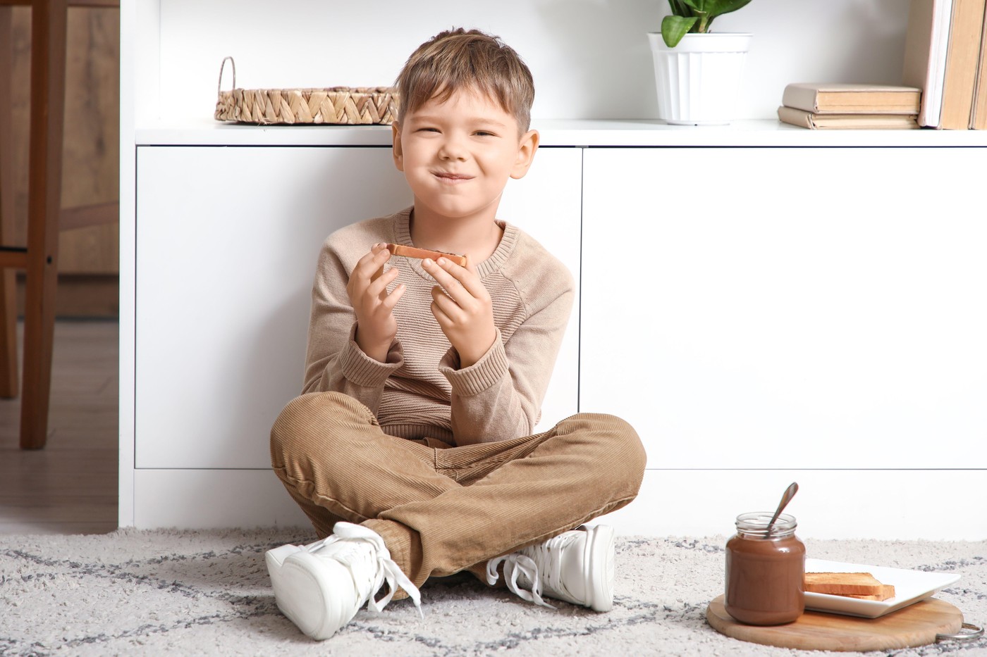 otrok sedi na tleh in je kruh s čokoladnim namazom