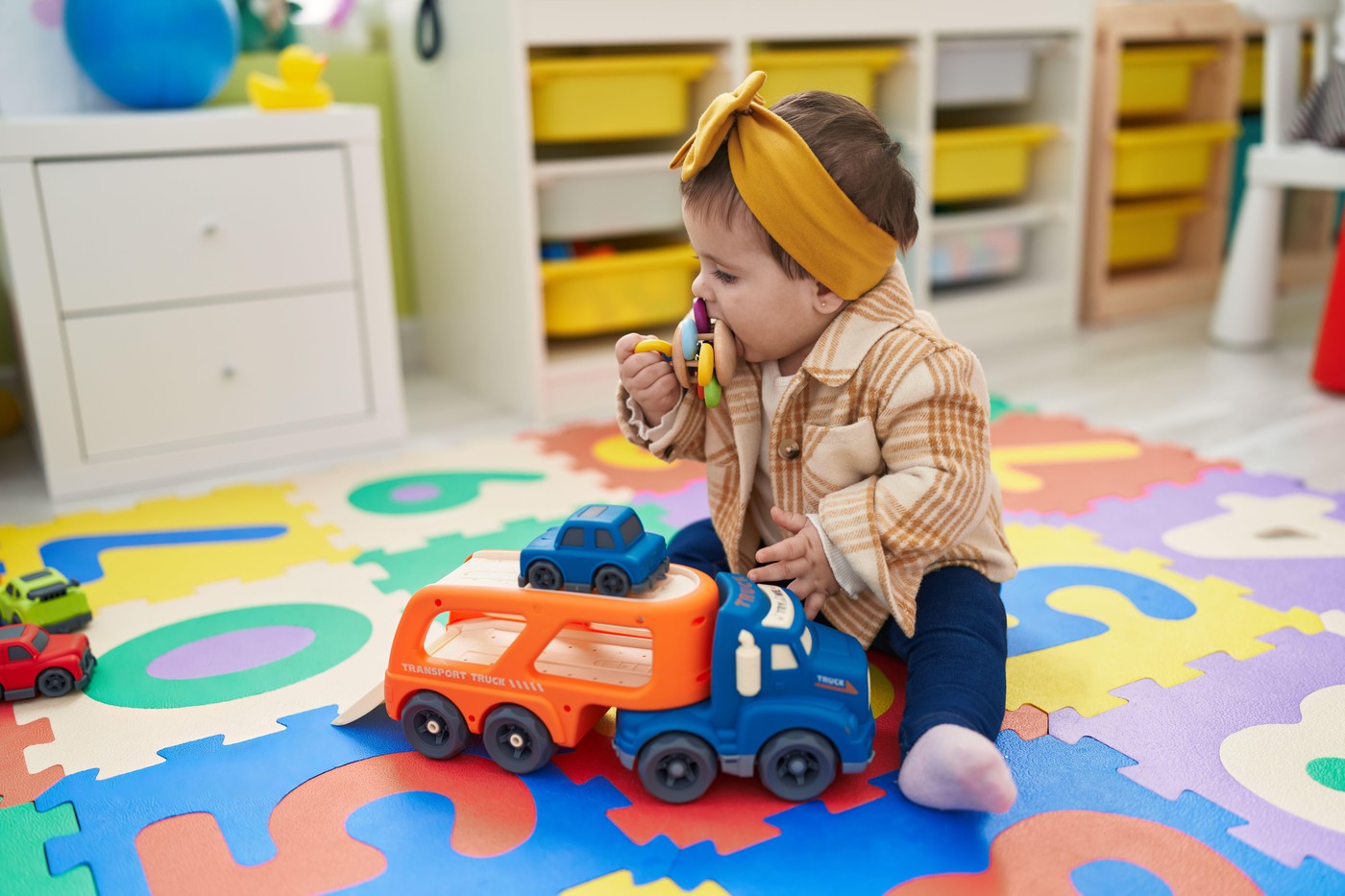 malček sedi na tleh in daje igračo v usta