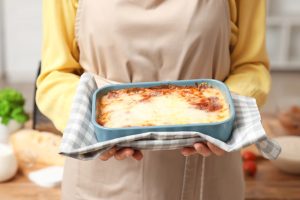 ženska v rokah drži pekač z lazanjo