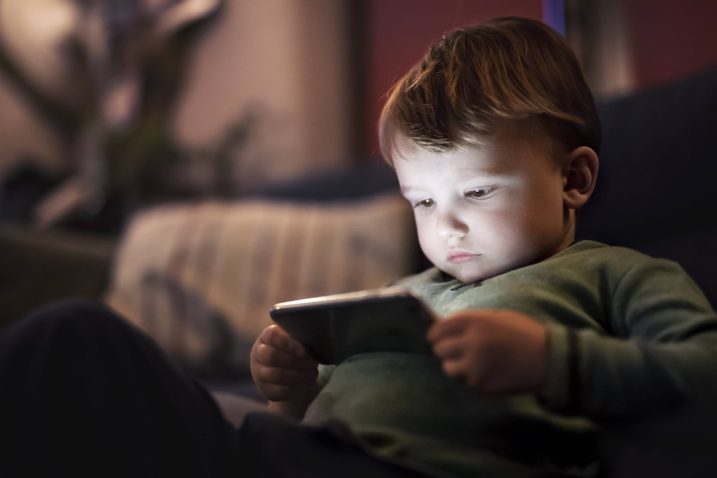 deček sedi na postelji in gleda vsebino na telefonu