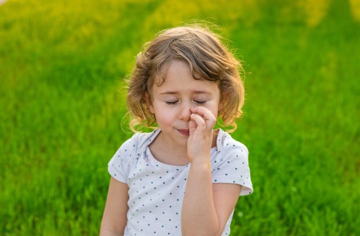deklica stoji na travniku in si brska po nosu