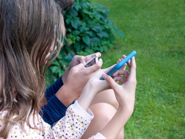 deklici sedita na prostem in gledata vsaka svoj telefon