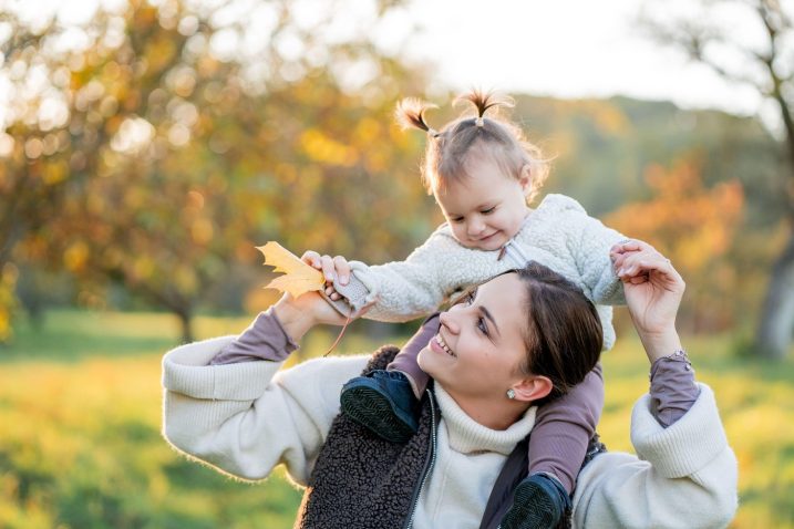 mlada mamica na sprehodu nosi hčerko na ramenih