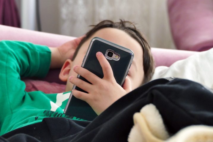mlajši otrok leži na postelji in gleda v telefon