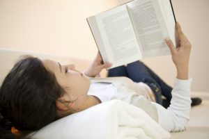najstnica leži na postelji in bere knjigo