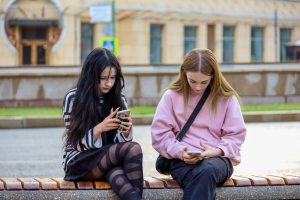 najstnici sedita na klopi v mestu s telefonoma v rokah