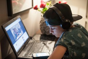 najstnik igra igrice na telefoni in je hkrati na računalniku, s slušalkami na glavi