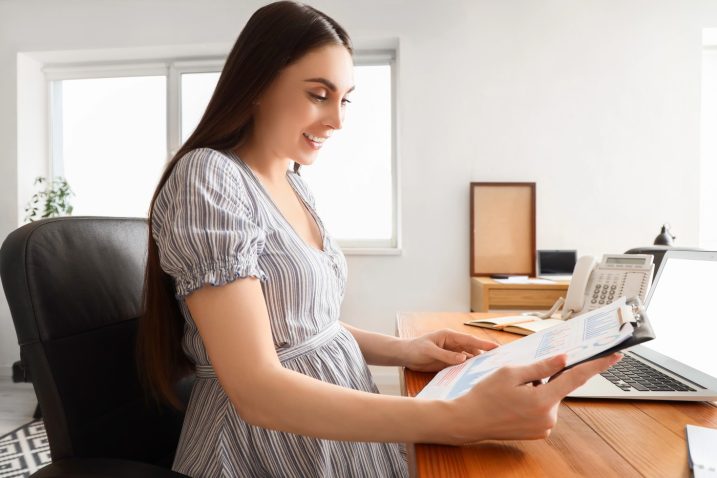 nosečnica sedi za mizo v službi z dokumenti v roki
