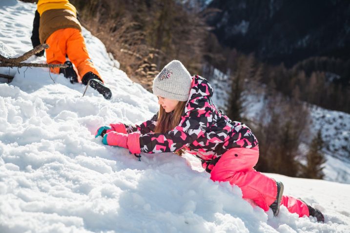 otroci, oblečeni v kombinezone, se igrajo na snegu na tleh