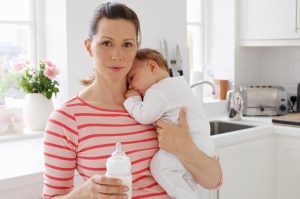 mama drži v naročju otroka in stekleničko v roki