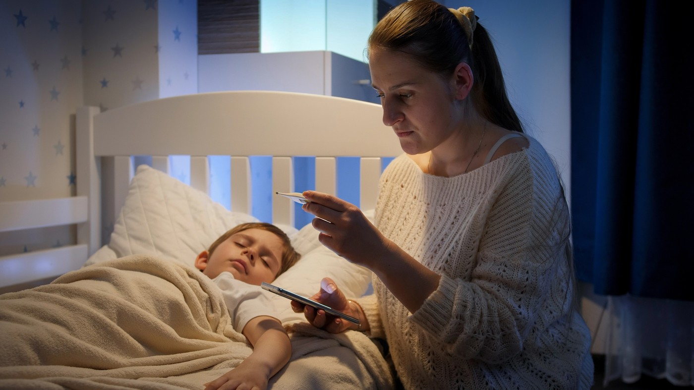 mama meri vročino otroku, v rokah ima telefon