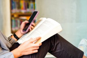 oseba uporablja telefon, medtem ko bere knjigo