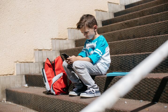 otrok sedi zunaj na stopnicah s telefonom v roki